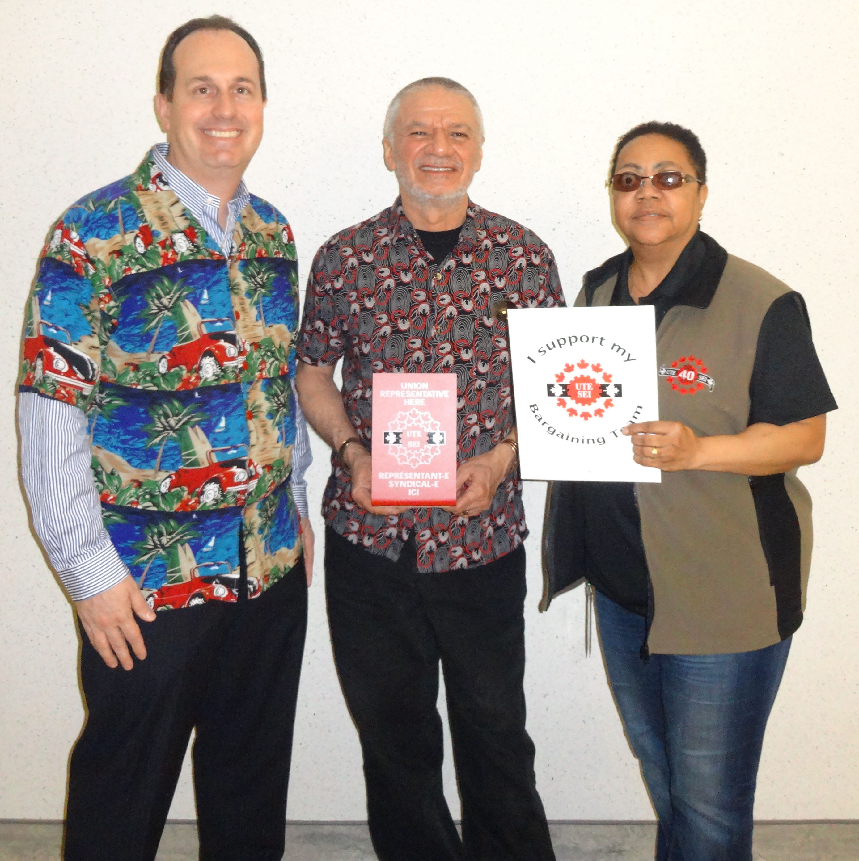 Ryan Ward, Mani Mifsud et Vona Martin posant avec les panneaux SEI et habillés dans les couleurs du syndicat et des couleurs vives pour notre journée de "Célébration"