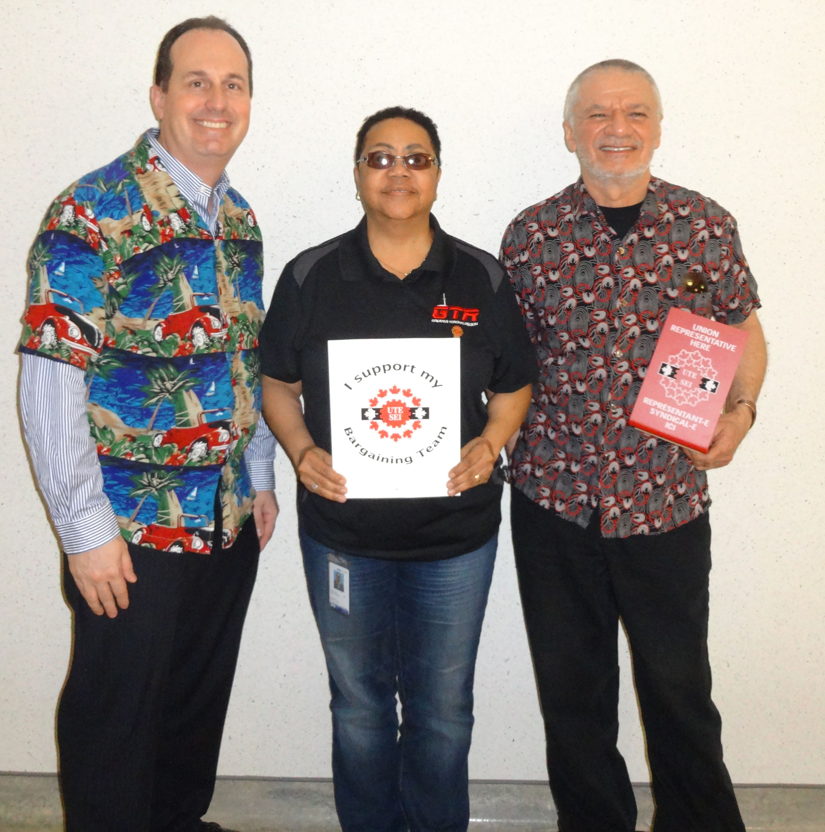 Ryan Ward, Mani Mifsud et Vona Martin posant avec les panneaux SEI et habillés dans les couleurs du syndicat et des couleurs vives pour notre journée de "Célébration"