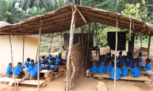 children in school uniforms sitting on benches in an outdoor school